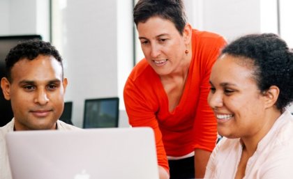 Two university students looking at laptop while lecturer looks over their shoulder. Image, UQ
